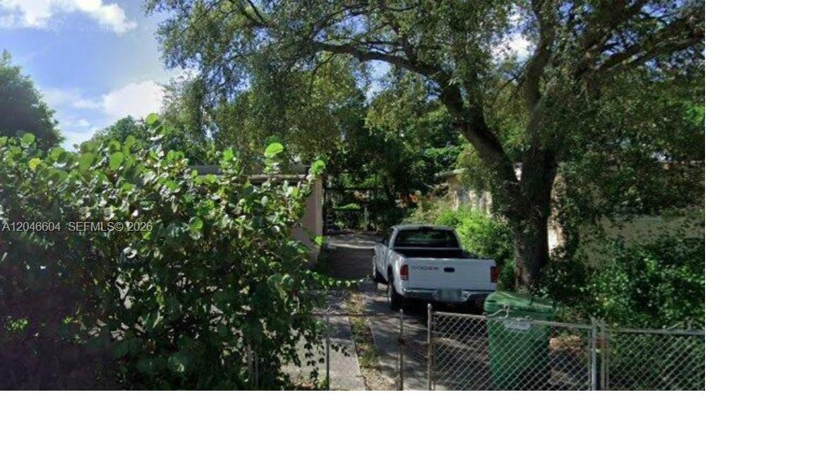 A white pickup truck is parked in a driveway next to a house and trees — OPA-LOCKA, FL