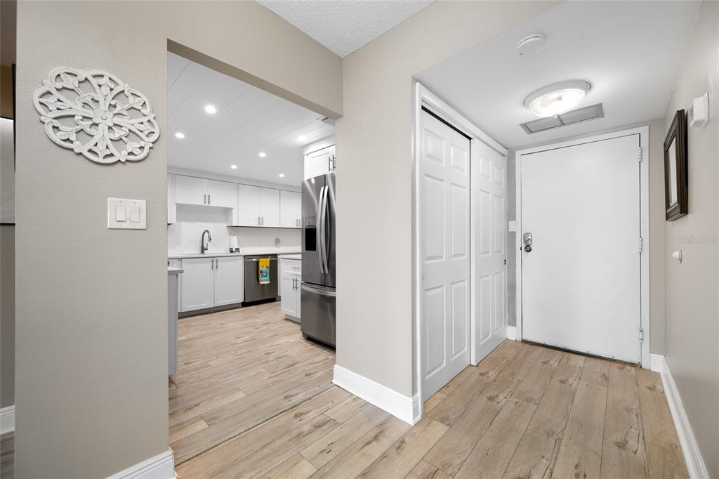 An entryway with wood-look flooring leads into a modern kitchen with white cabinets — 1621 GULF BOULEVARD UNIT 706, CLEARWATER BEACH, FL