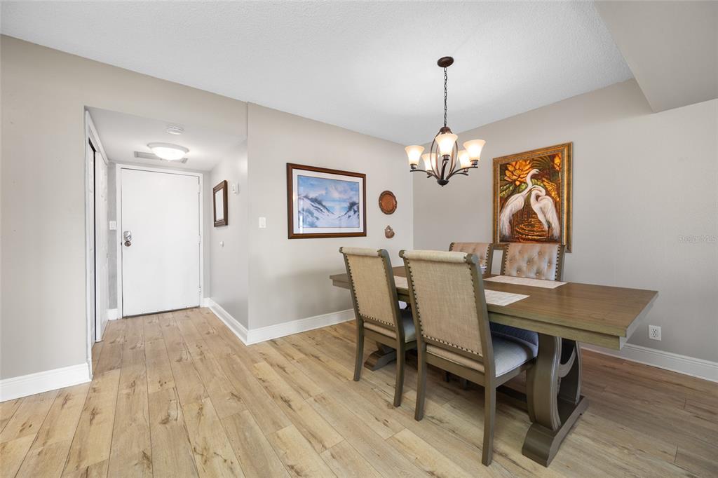 A dining room features a wooden table, upholstered chairs, a chandelier, and light wood flooring — 1621 GULF BOULEVARD UNIT 706, CLEARWATER BEACH, FL