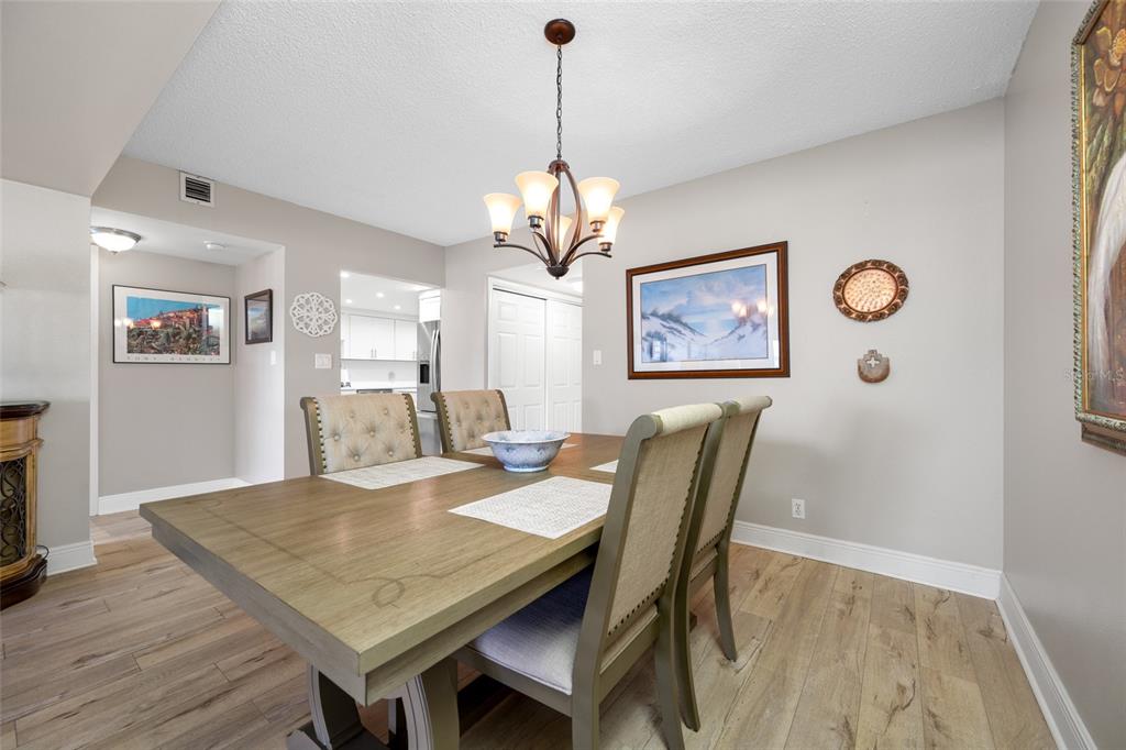 A dining room features a wooden table, upholstered chairs, a chandelier, and light wood flooring — 1621 GULF BOULEVARD UNIT 706, CLEARWATER BEACH, FL