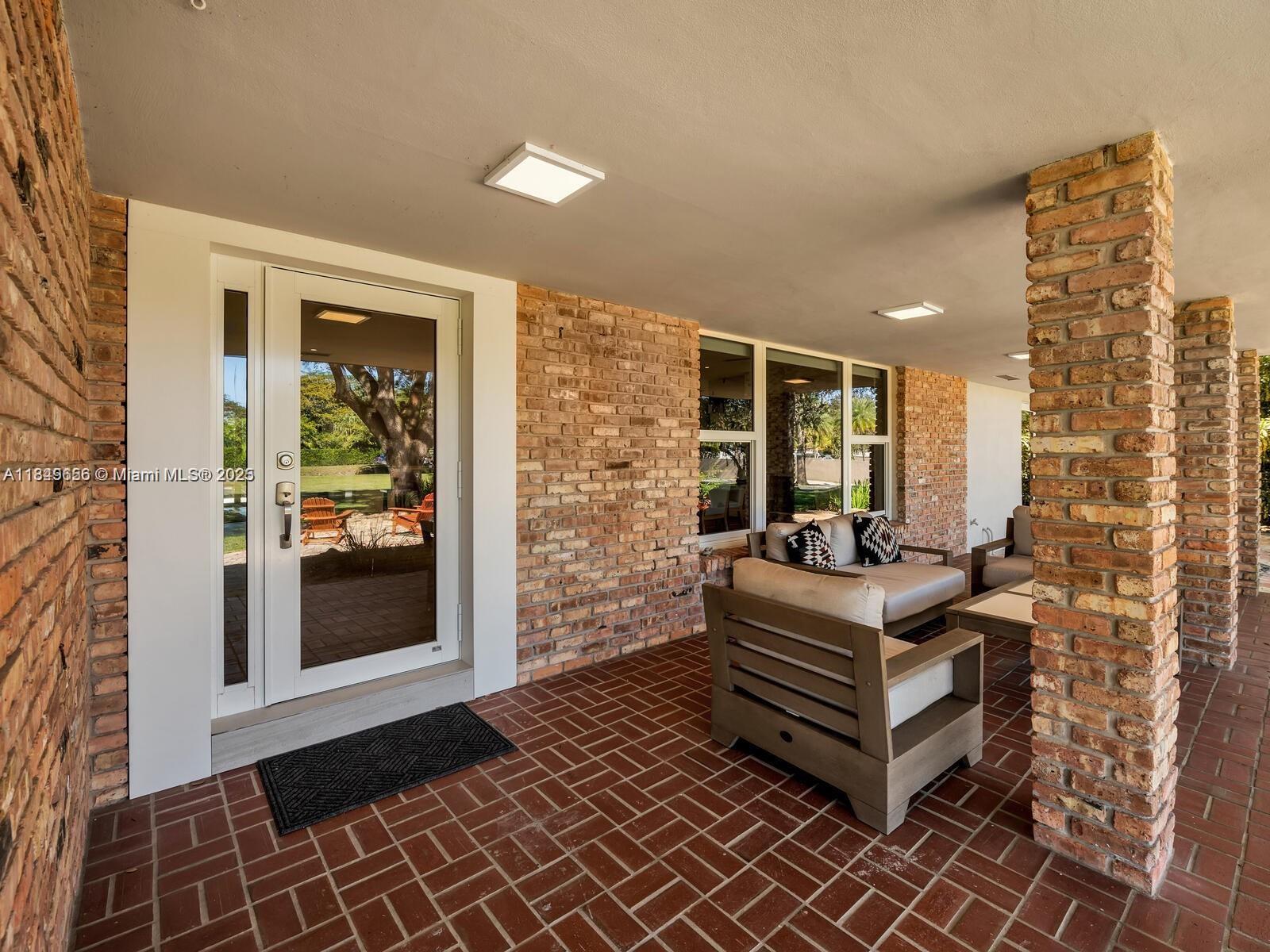 A covered brick patio features a glass-paneled door, brick columns, and outdoor lounge furniture — 13350 Luray Rd, Southwest Ranches FL 33330, SOUTHWEST RANCHES, FL