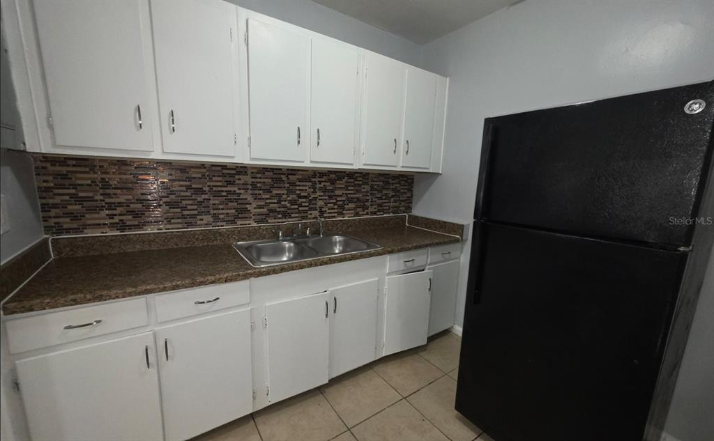 A kitchen features white cabinets, a brown speckled countertop, a tiled backsplash, and a black refrigerator — 1816 E 27TH STREET, JACKSONVILLE, FL