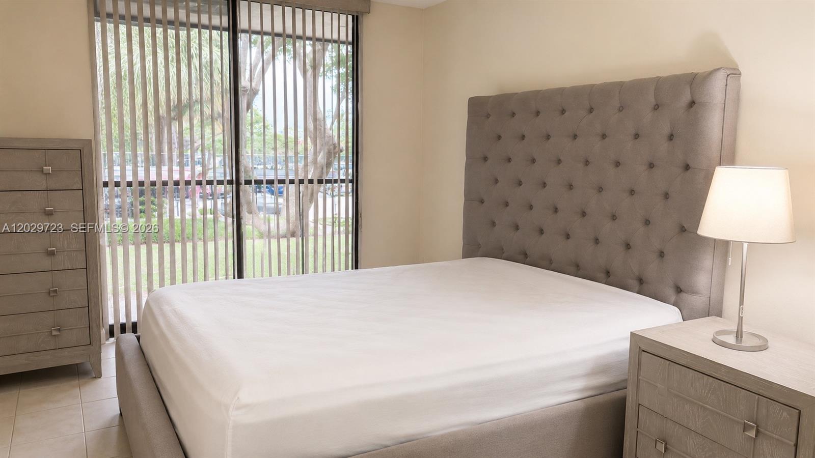 A bedroom features a tufted gray headboard, matching furniture, and a sliding glass door — 8520 SW 133rd Ave Rd # 210, Miami FL 33183, MIAMI, FL