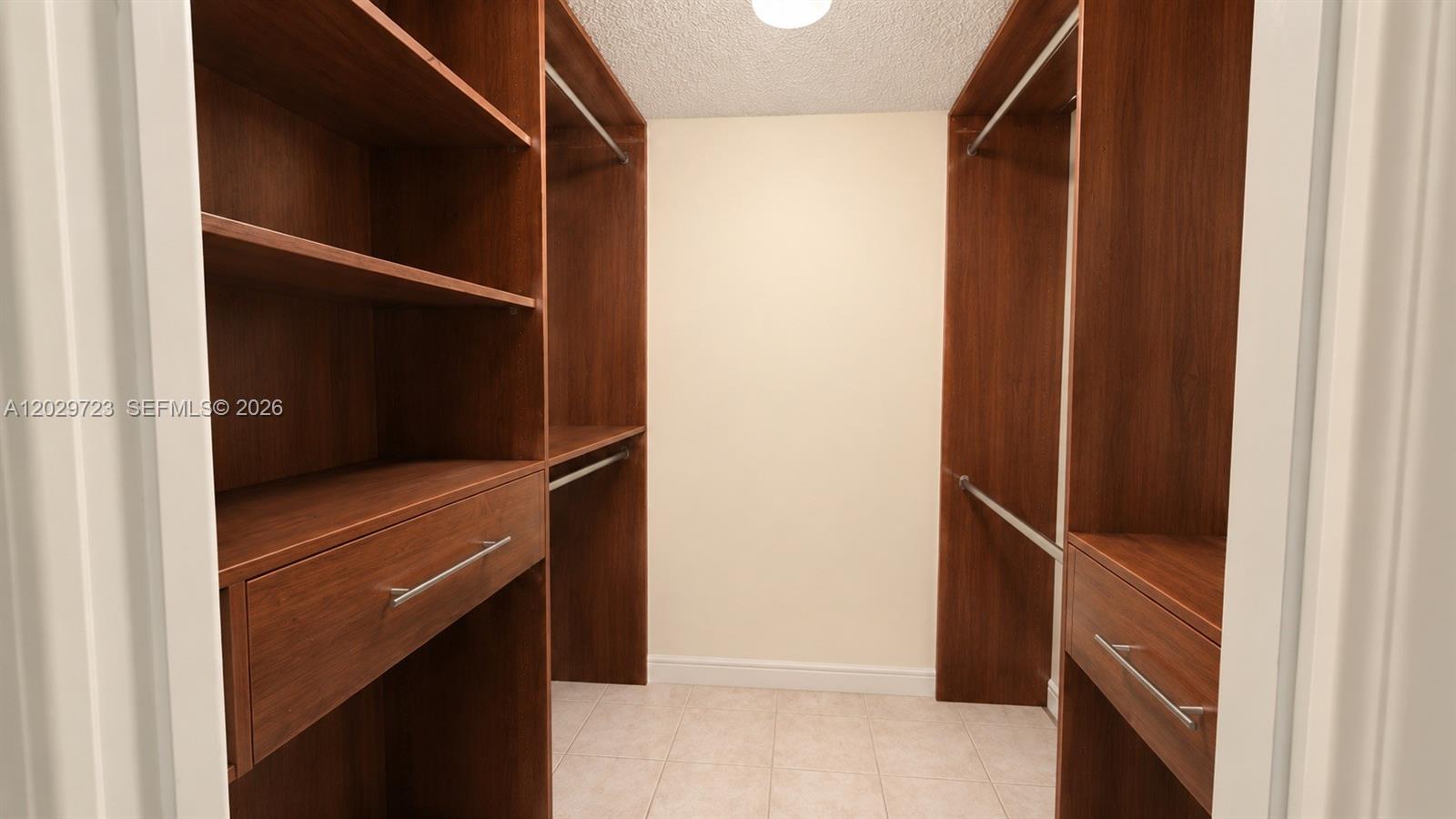 A walk-in closet features dark wood shelving, hanging rods, and drawers on tiled flooring — 8520 SW 133rd Ave Rd # 210, Miami FL 33183, MIAMI, FL