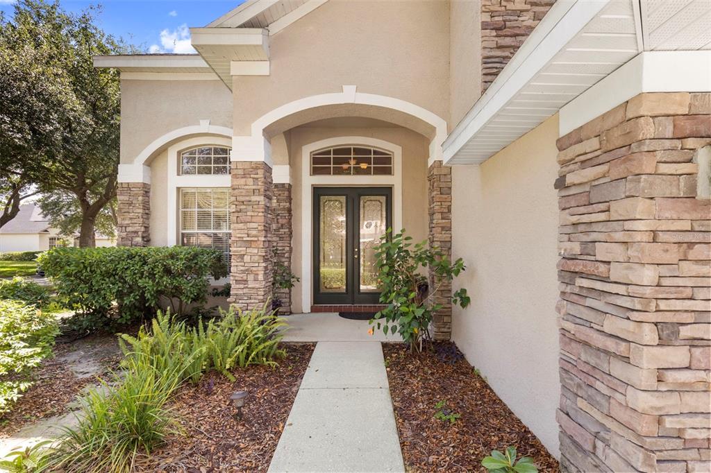 A front entryway features a stone-accented facade, a concrete walkway, and double glass doors — 17823 ARBOR CREEK DRIVE, TAMPA, FL