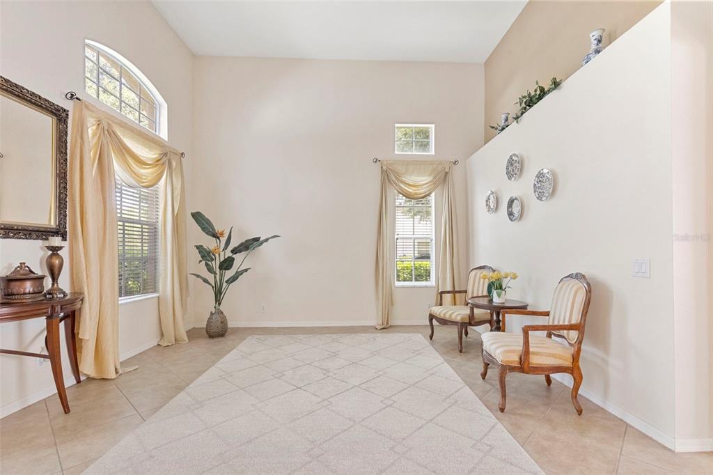 A bright living room features high ceilings, tile floors, two windows with drapes, and chairs — 17823 ARBOR CREEK DRIVE, TAMPA, FL