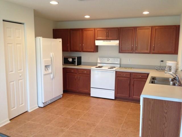 A kitchen features wood cabinets, white appliances, a tiled floor, and a double-door pantry — 5109 BUTTERFLY SHELL DRIVE, APOLLO BEACH, FL