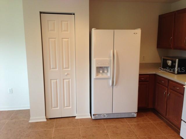 A kitchen features a white side-by-side refrigerator, wood cabinets, and a white bi-fold door — 5109 BUTTERFLY SHELL DRIVE, APOLLO BEACH, FL