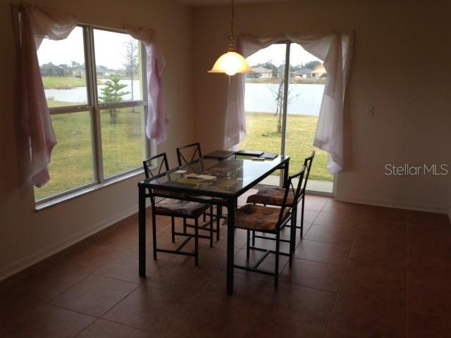 A dining area with a glass-top table, tile flooring, and large windows overlooking a lake — 5109 BUTTERFLY SHELL DRIVE, APOLLO BEACH, FL