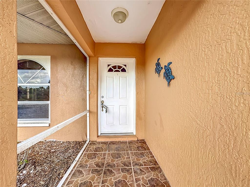 A covered entryway features a white front door, tiled flooring, and two decorative wall turtles — 1570 S BISCAYNE DRIVE, NORTH PORT, FL