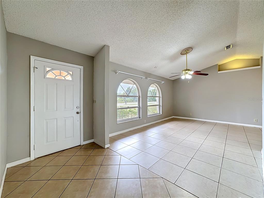 An empty room features beige tile flooring, vaulted ceilings, arched windows, and a ceiling fan — 1570 S BISCAYNE DRIVE, NORTH PORT, FL