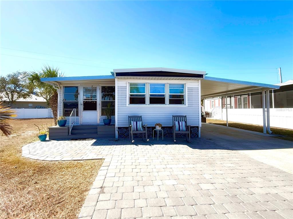 A light blue mobile home features a paved patio, two rocking chairs, and a carport — 308 S PORT ROYAL LANE, APOLLO BEACH, FL