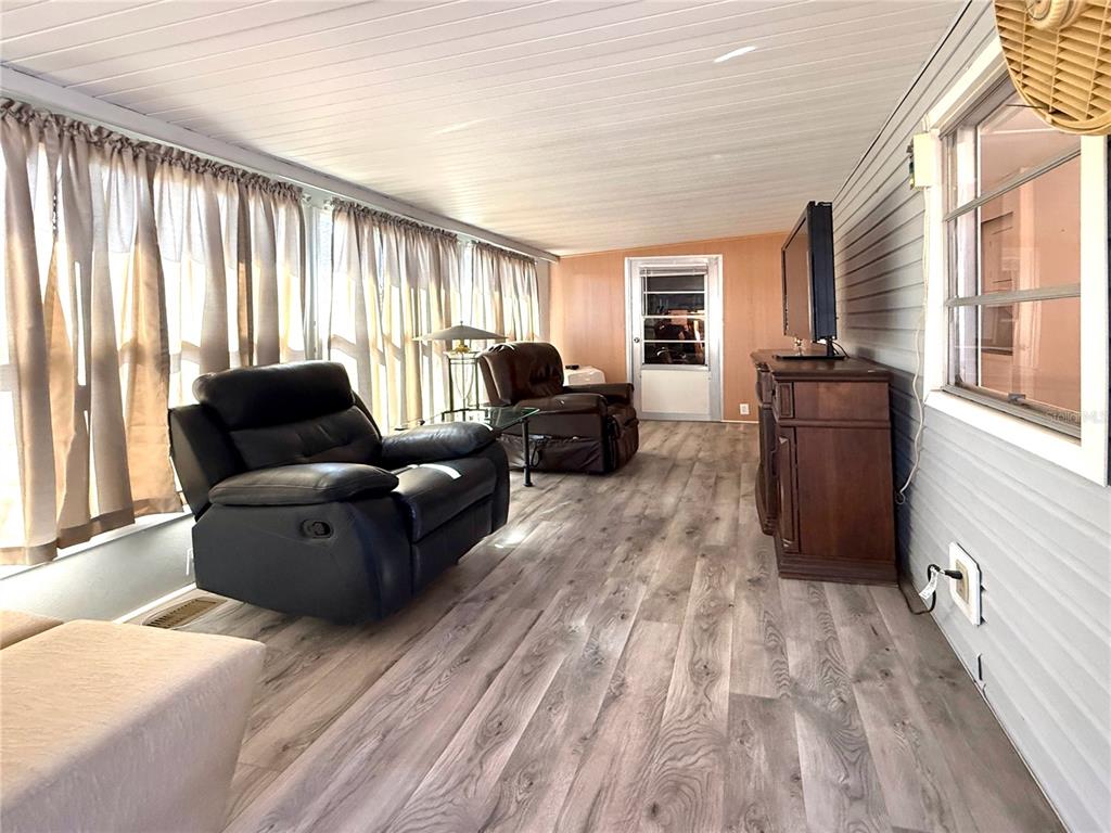 A sunroom features wood-look flooring, two leather recliners, a television on a cabinet, and curtains — 308 S PORT ROYAL LANE, APOLLO BEACH, FL