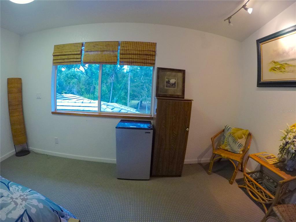 A bedroom features a window with bamboo shades, a small refrigerator, and wicker furniture — 18620 WAYNE ROAD UNIT 1, ODESSA, FL