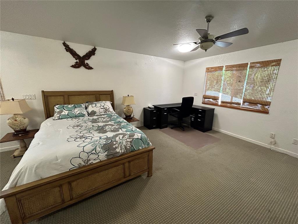 A bedroom features a wooden bed, a black desk, and a ceiling fan — 18620 WAYNE ROAD UNIT 1, ODESSA, FL