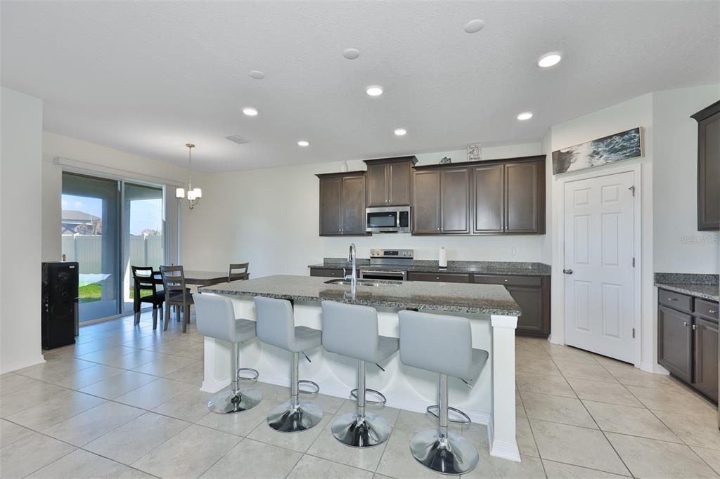 A kitchen features dark wood cabinets, granite countertops, a central island, and tile flooring — 2927 MARINE GRASS DRIVE, WIMAUMA, FL