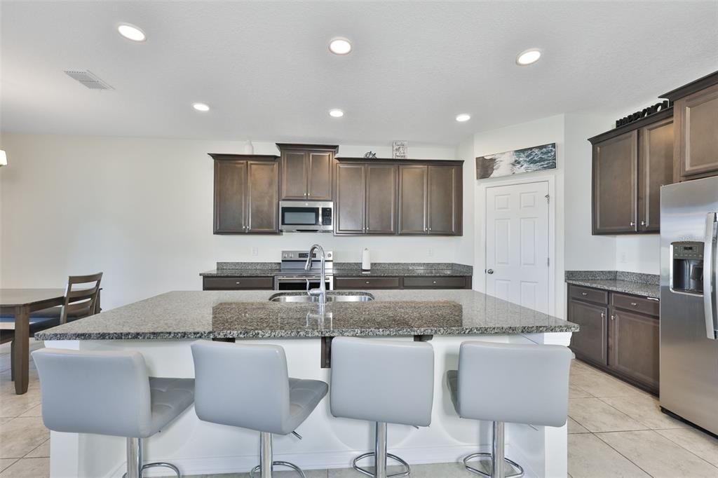 A kitchen features dark wood cabinets, granite countertops, a large island, and four gray stools — 2927 MARINE GRASS DRIVE, WIMAUMA, FL