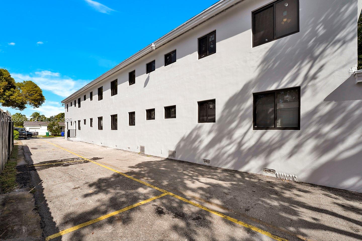 A long, white, multi-story building exterior features numerous dark-framed windows above a paved parking lot — 2150 SW 26th St # 7, Miami FL 33133, MIAMI, FL