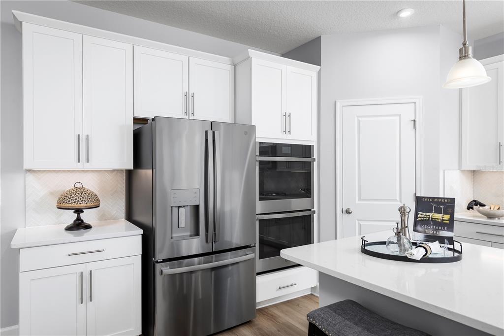 A modern kitchen features white cabinets, stainless steel appliances, and a white quartz island countertop — 7460 SW 107TH LANE, OCALA, FL