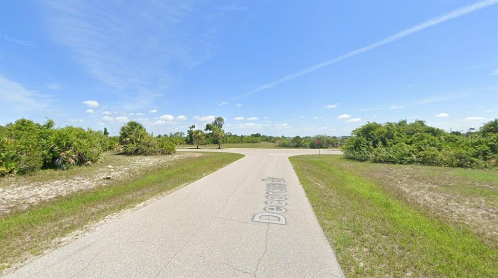 A paved road leads to a T-intersection in a grassy, undeveloped area with scattered trees — 39 DECORORE DRIVE, ROTONDA WEST, FL