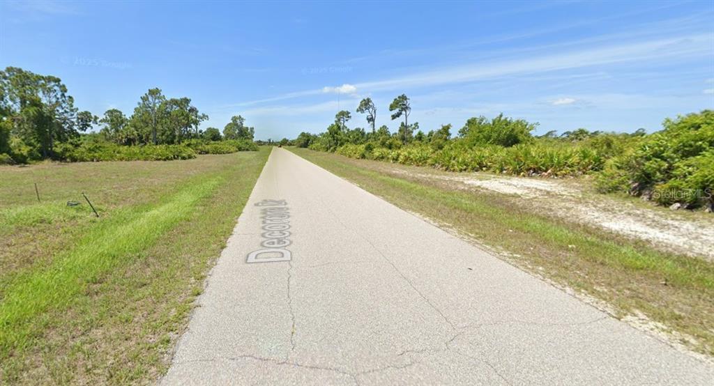 A paved road stretches through a rural, undeveloped area with grassy fields and scattered trees — 39 DECORORE DRIVE, ROTONDA WEST, FL