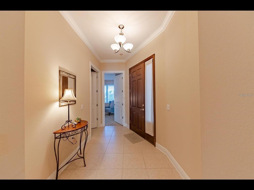 A tiled entryway features a wooden front door, a console table, and a light fixture — 1042 BELLASOL WAY UNIT 203, APOLLO BEACH, FL