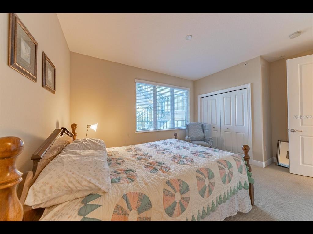A bedroom features a wooden bed frame, a patterned quilt, a window, and a closet — 1042 BELLASOL WAY UNIT 203, APOLLO BEACH, FL