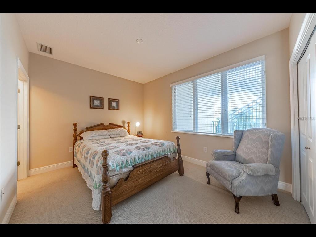 A bedroom features a wooden bed, a patterned armchair, and large windows with white blinds — 1042 BELLASOL WAY UNIT 203, APOLLO BEACH, FL