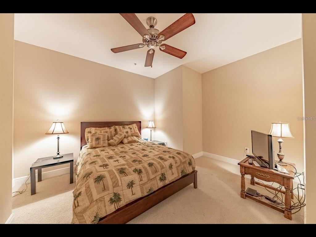 A bedroom features a bed with palm-print bedding, a ceiling fan, and two bedside lamps — 1042 BELLASOL WAY UNIT 203, APOLLO BEACH, FL