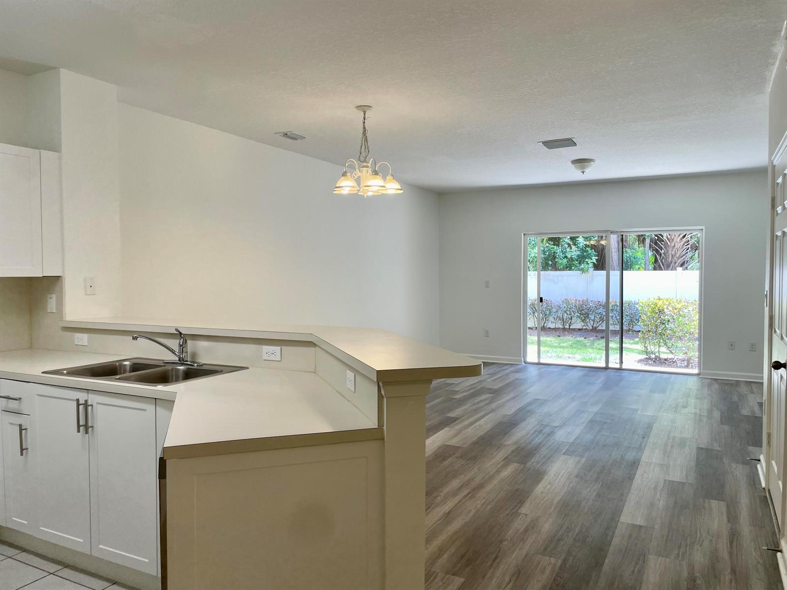 A kitchen with white cabinets and a breakfast bar overlooks a living area with flooring — 5064 SE Mariner Garden Circle, Stuart FL 34997, STUART, FL