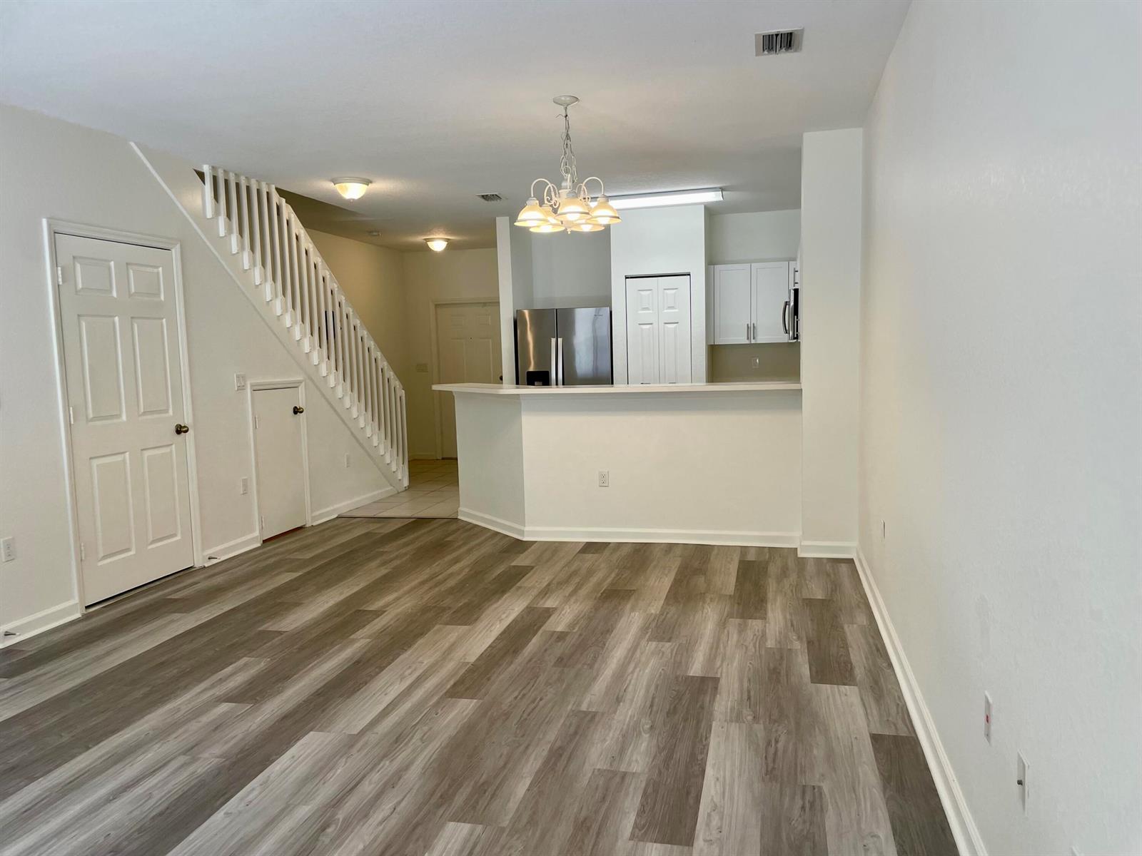 A living room with wood-look flooring, a staircase, and an open kitchen with a breakfast bar — 5064 SE Mariner Garden Circle, Stuart FL 34997, STUART, FL