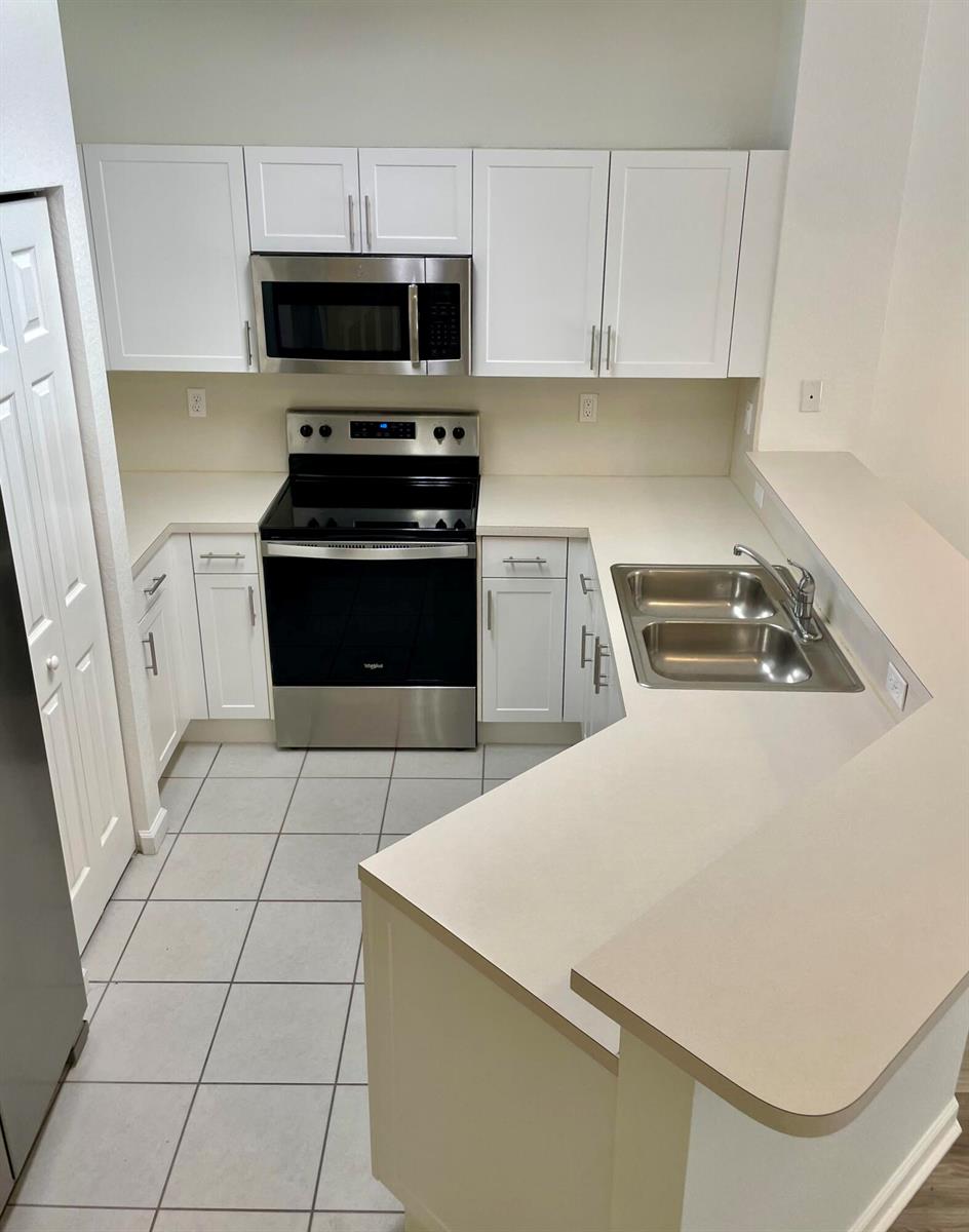 A kitchen features white cabinets, stainless steel appliances, and a light-colored countertop with a sink — 5064 SE Mariner Garden Circle, Stuart FL 34997, STUART, FL