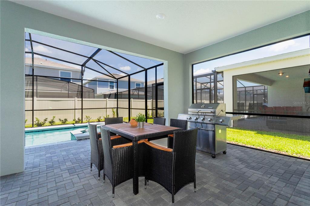 A covered patio features a dining set, a stainless steel grill, and a screened-in pool — 3344 LILAC WAY, DAVENPORT, FL