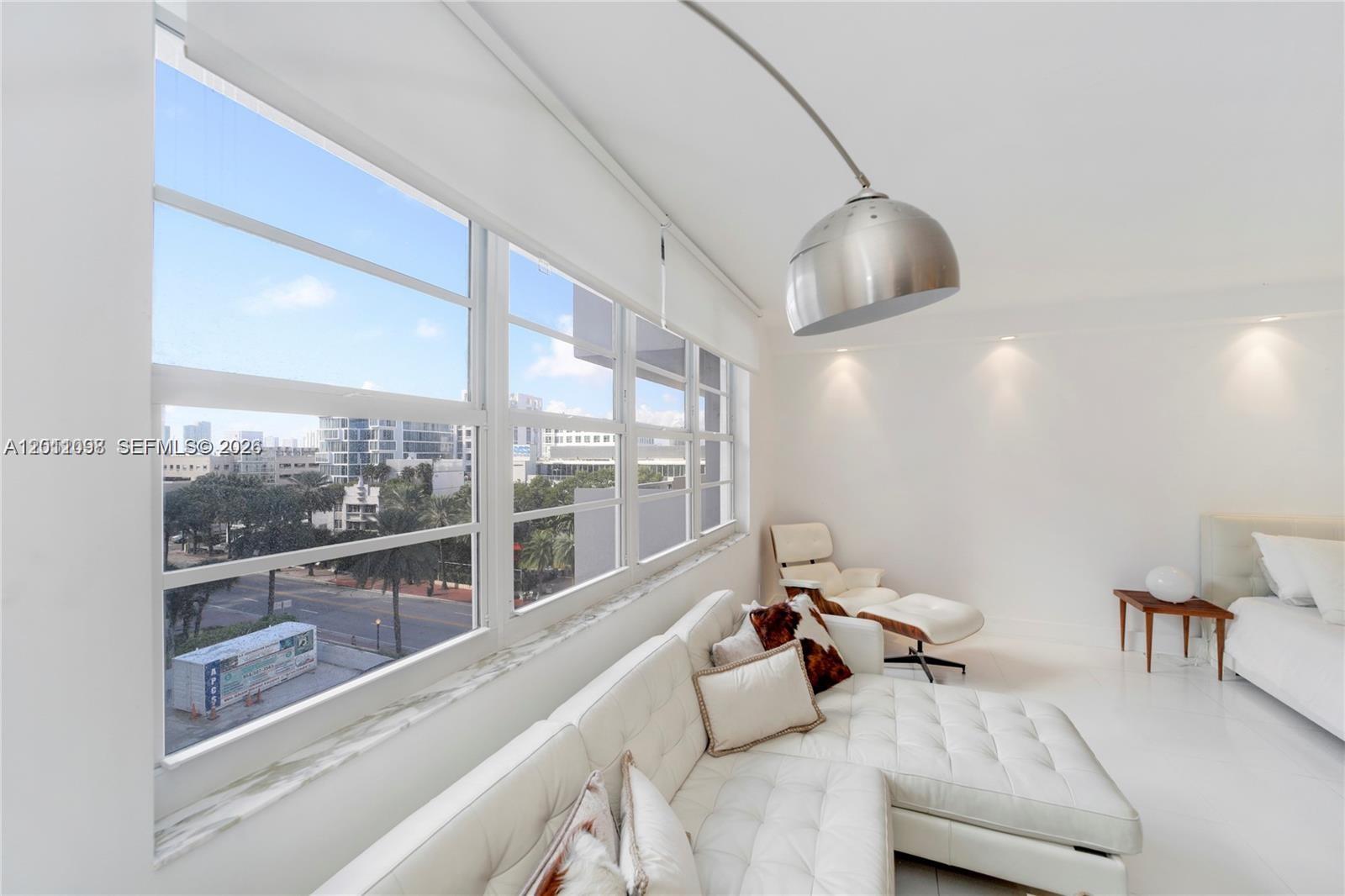 A bright living room features a white tufted sectional, a lounge chair, and large windows — 100 Lincoln Rd # 605, Miami Beach FL 33139, MIAMI BEACH, FL