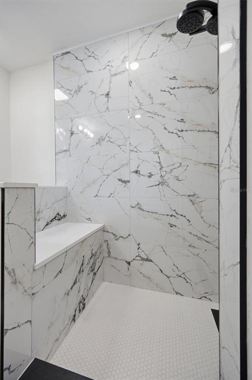 A walk-in shower features white marble-look wall tiles, a built-in bench, and a hexagonal tile floor — 7242 LYNNWOOD AVENUE N, ST PETERSBURG, FL