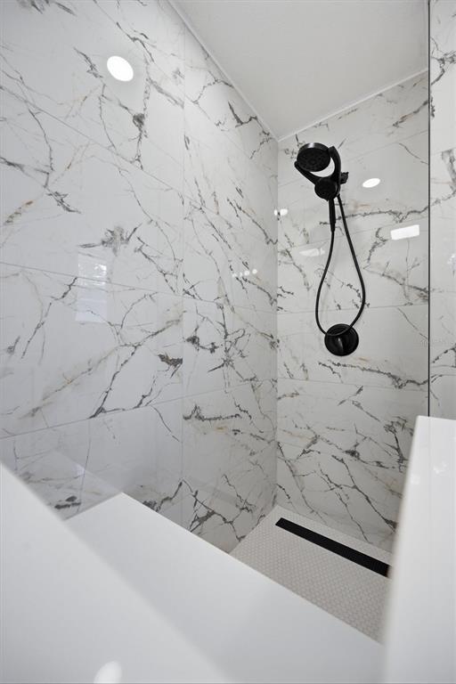 A walk-in shower features white marble-patterned wall tiles, a black handheld showerhead, and mosaic flooring — 7242 LYNNWOOD AVENUE N, ST PETERSBURG, FL