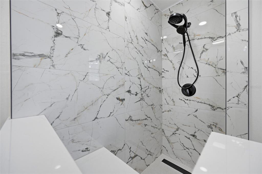A walk-in shower features white marble-look wall tiles, a black handheld showerhead, and a drain — 7242 LYNNWOOD AVENUE N, ST PETERSBURG, FL