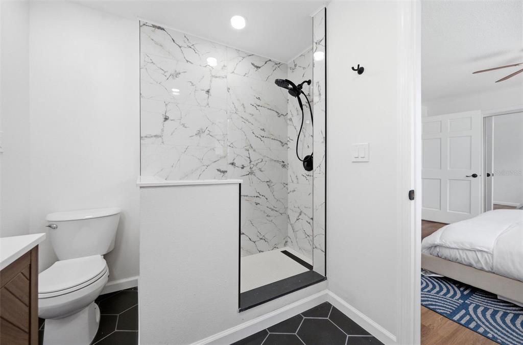 A bathroom features a marble-tiled walk-in shower, black hexagonal floor tiles, and a white toilet — 7242 LYNNWOOD AVENUE N, ST PETERSBURG, FL
