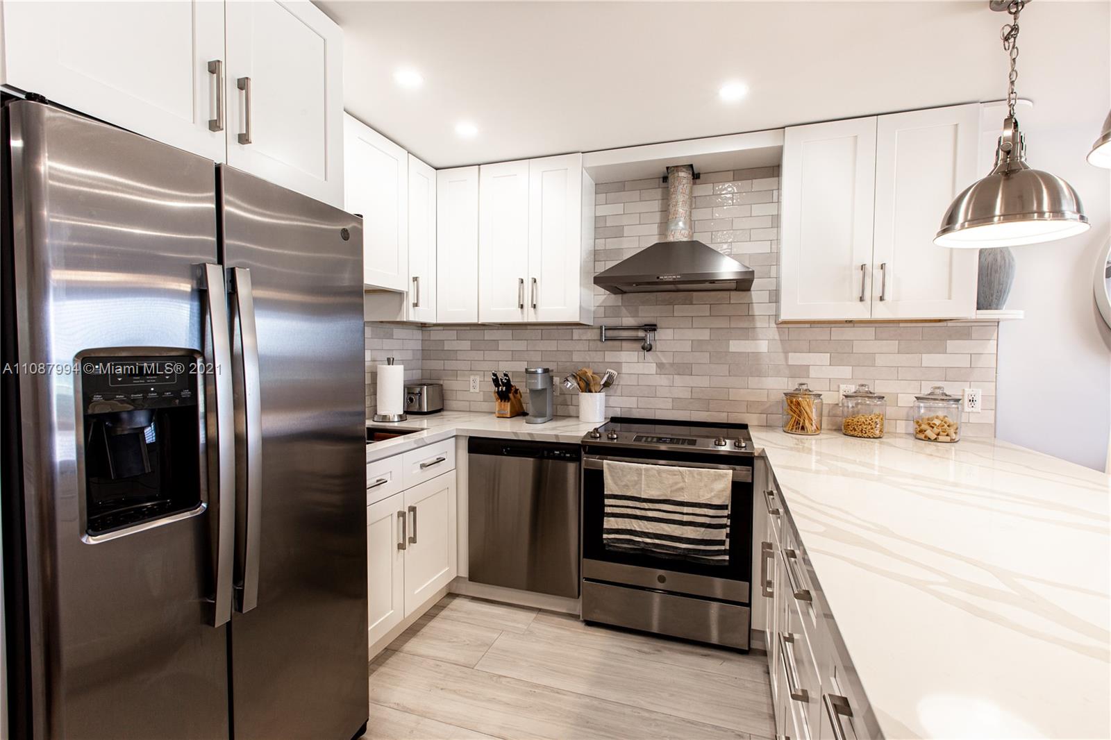 A modern kitchen features white cabinetry, stainless steel appliances, and a light-colored stone countertop — 300 Oregon St # 204, Hollywood FL 33019, HOLLYWOOD, FL