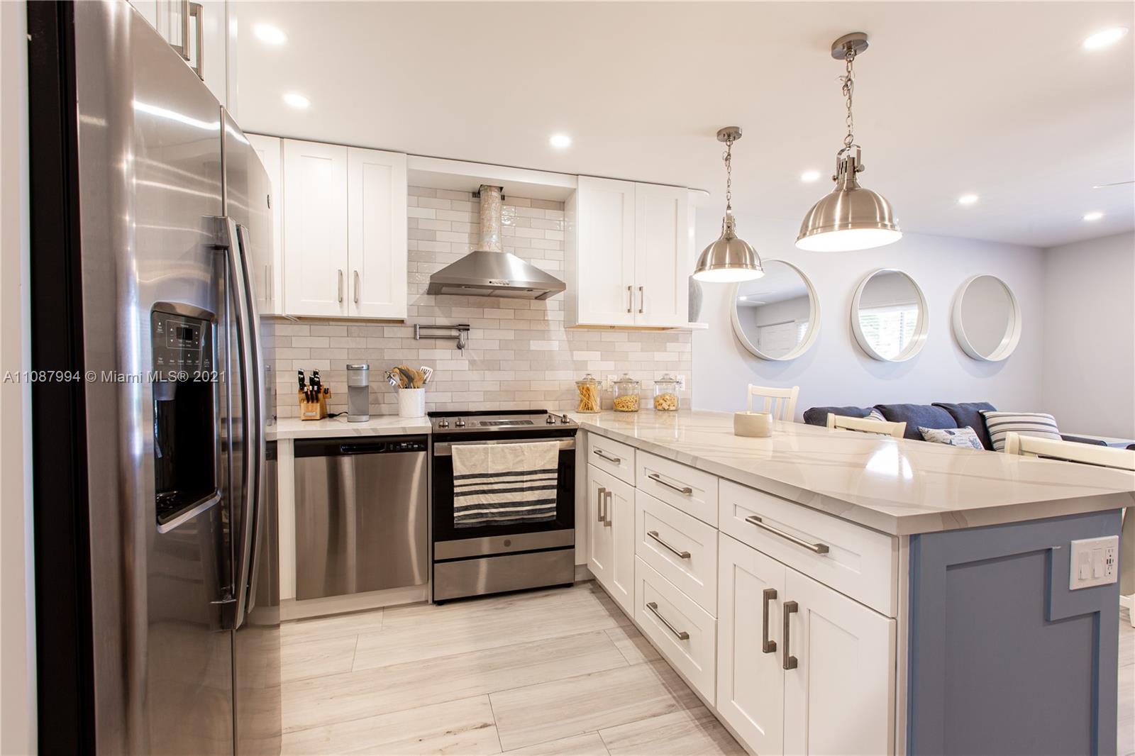 A modern kitchen features white cabinets, stainless steel appliances, a blue island, and subway tile — 300 Oregon St # 204, Hollywood FL 33019, HOLLYWOOD, FL