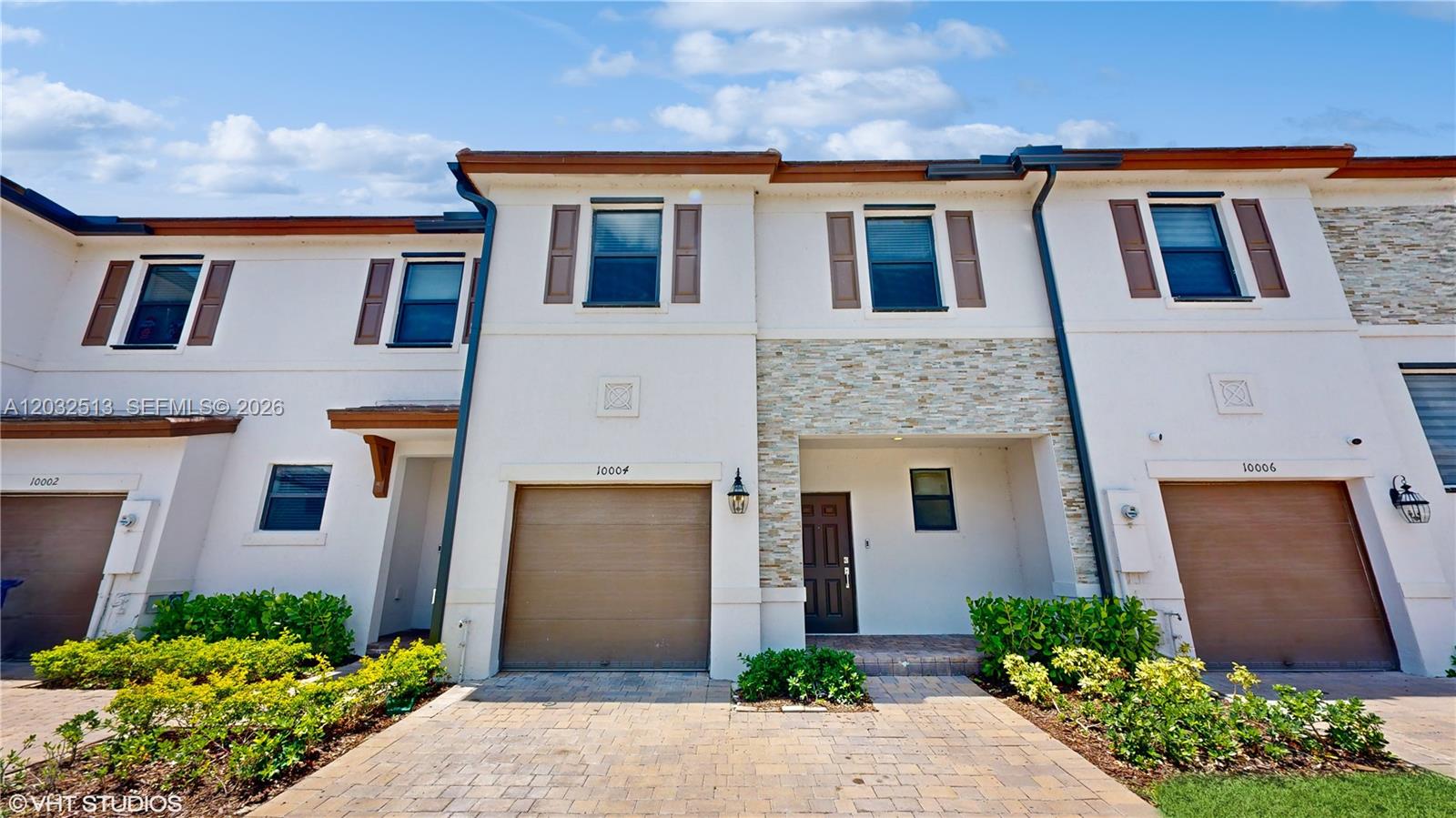 The exterior of a multi-unit townhouse features stucco walls, stone accents, and brown garage doors — 10004 SW 231 LN, Miami FL 33190, MIAMI, FL