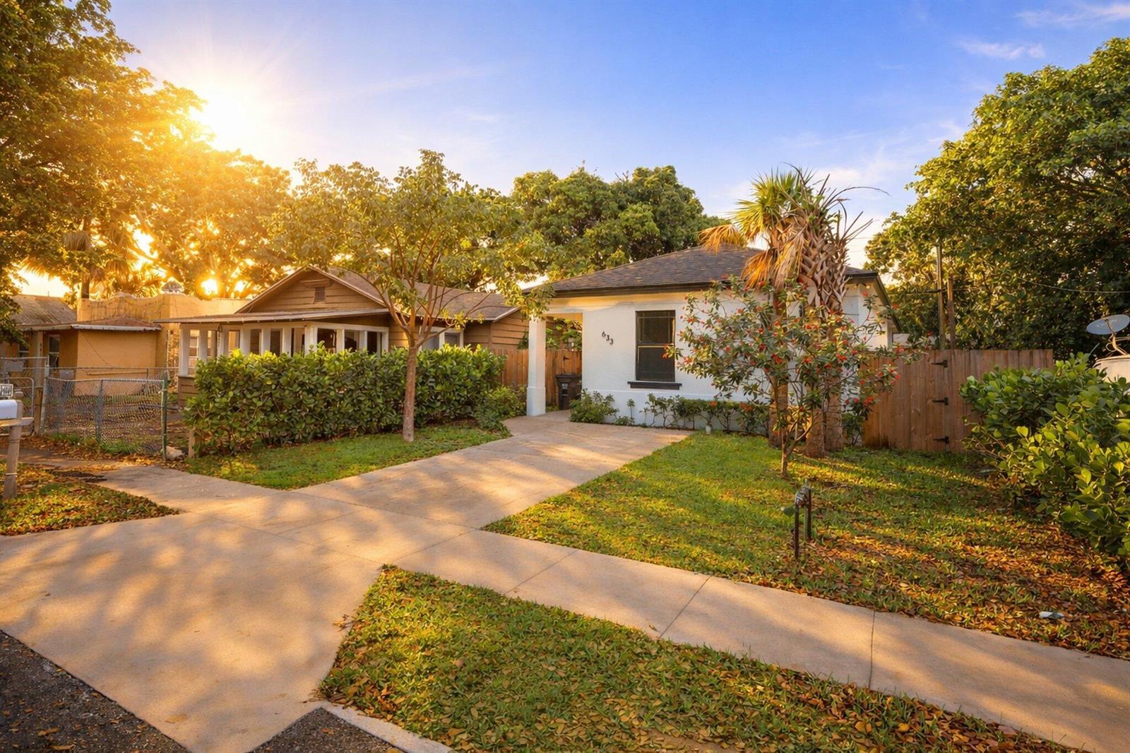 A white house with a concrete driveway and a front lawn under a sunny sky — 633 55th Street, West Palm Beach FL 33407, WEST PALM BEACH, FL