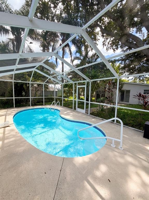 A kidney-shaped swimming pool sits inside a screened-in lanai with a concrete deck — 2119 W HENRY AVENUE, TAMPA, FL