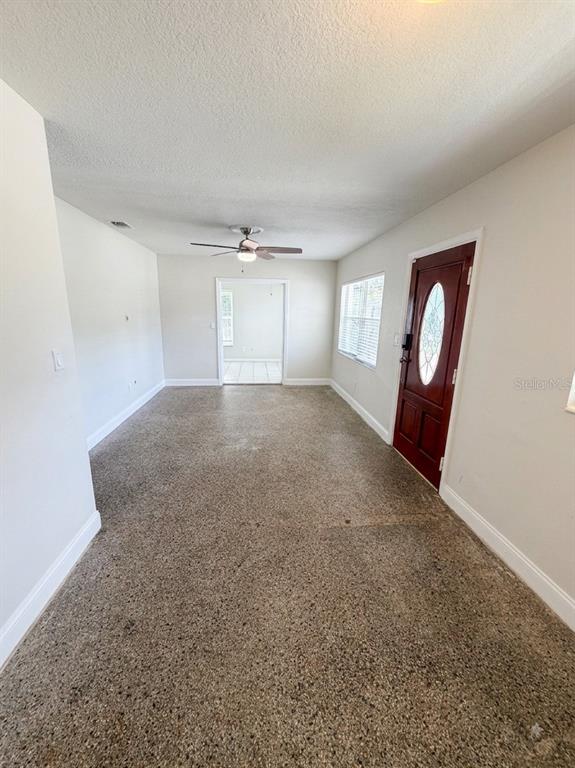 An interior view of a living room with terrazzo flooring, a ceiling fan, and a door — 2119 W HENRY AVENUE, TAMPA, FL