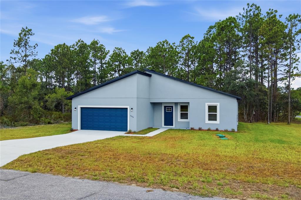 A single-story house with a blue garage door and front door sits on a grassy lot — 10708 N CALDERA AVENUE, CITRUS SPRINGS, FL