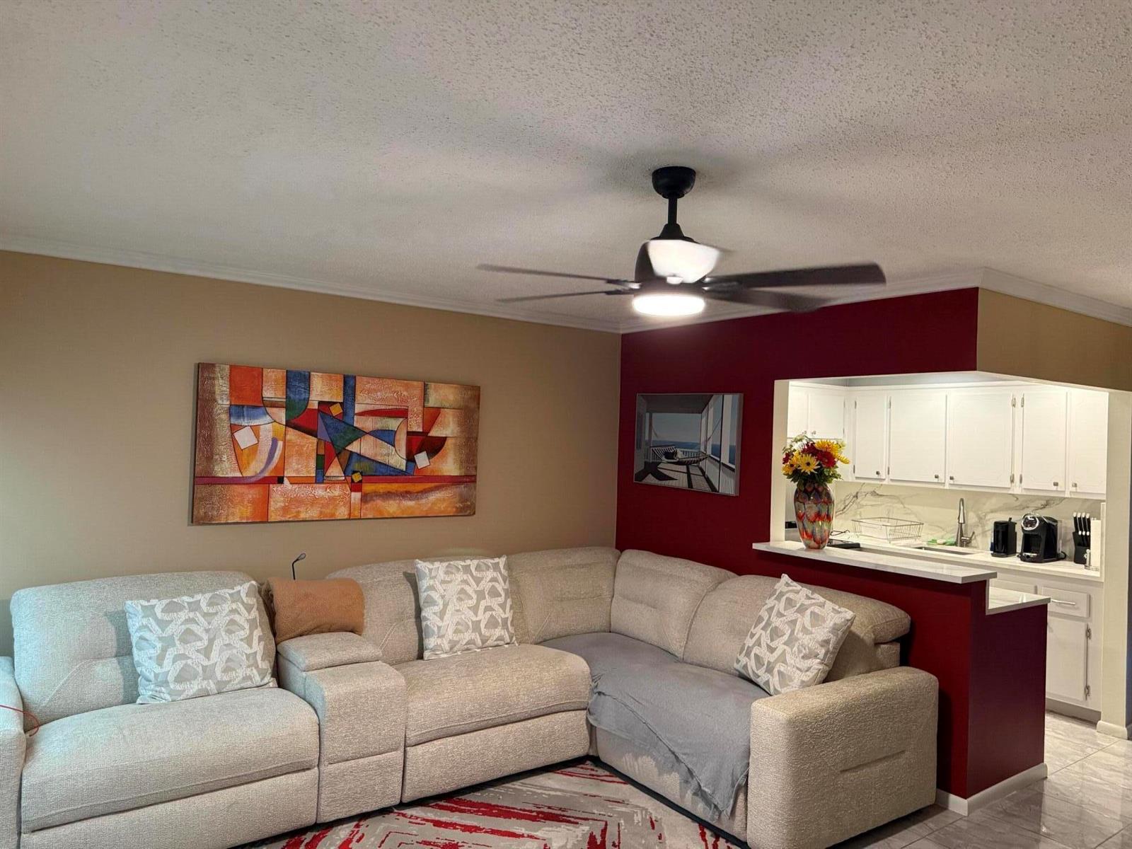 A living room features a beige sectional sofa, a ceiling fan, and a red accent wall — 362 Oakridge T, Deerfield Beach FL 33442, DEERFIELD BEACH, FL