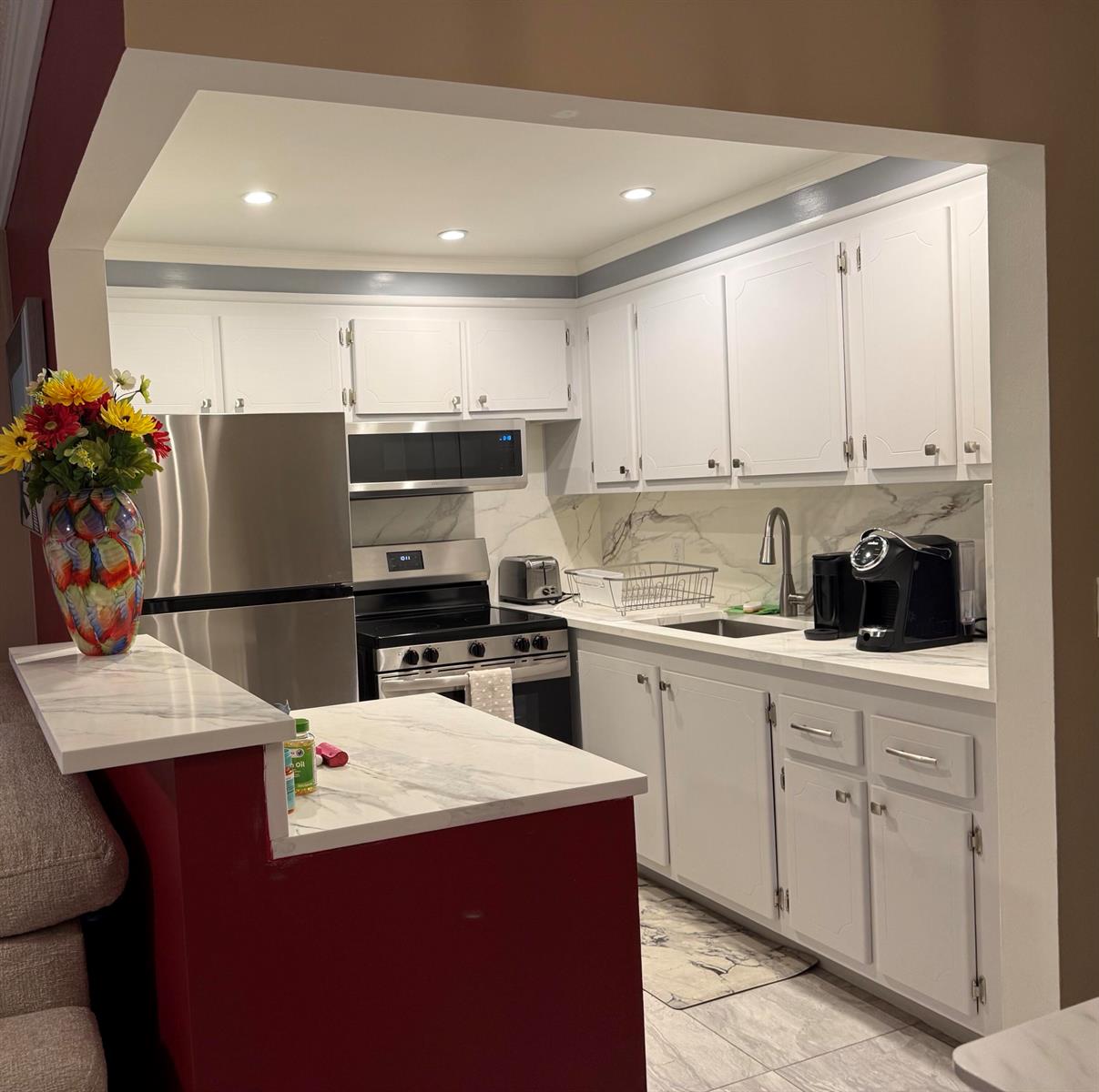 A kitchen features white cabinets, stainless steel appliances, and marble-look countertops with a red peninsula — 362 Oakridge T, Deerfield Beach FL 33442, DEERFIELD BEACH, FL