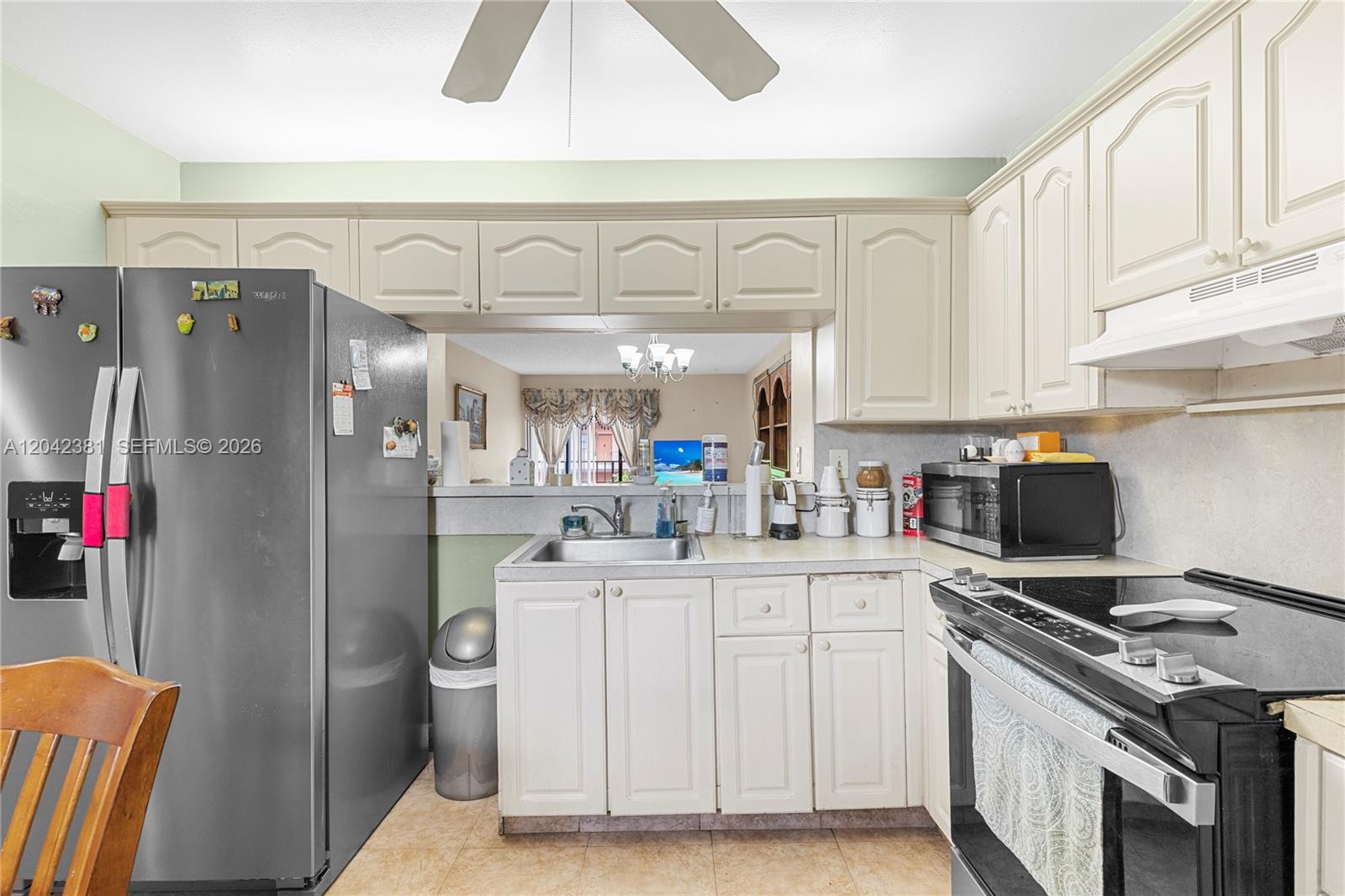 A kitchen features white cabinetry, stainless steel appliances, and a pass-through window to the living area — 1800 W 54th St # 209, Hialeah FL 33012, HIALEAH, FL