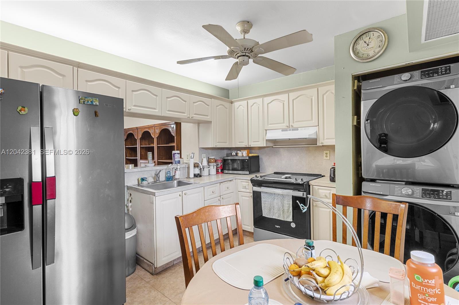 A kitchen features white cabinets, stainless steel appliances, a ceiling fan, and a stacked laundry unit — 1800 W 54th St # 209, Hialeah FL 33012, HIALEAH, FL