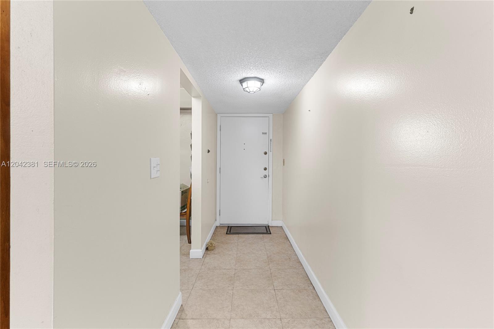A hallway with beige walls, tile flooring, and a white door at the end — 1800 W 54th St # 209, Hialeah FL 33012, HIALEAH, FL